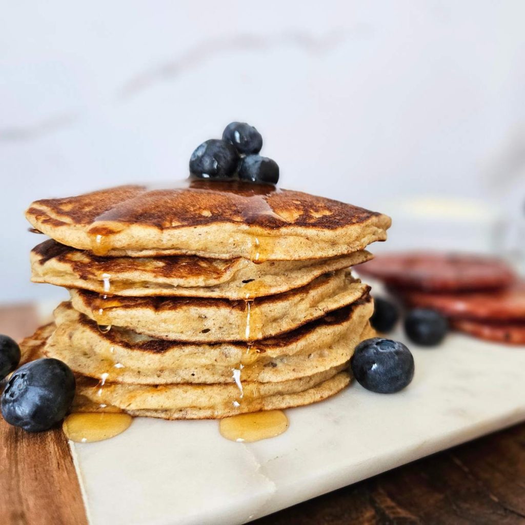A stack of einkorn pancakes with blueberries on top and syrup running down the sides