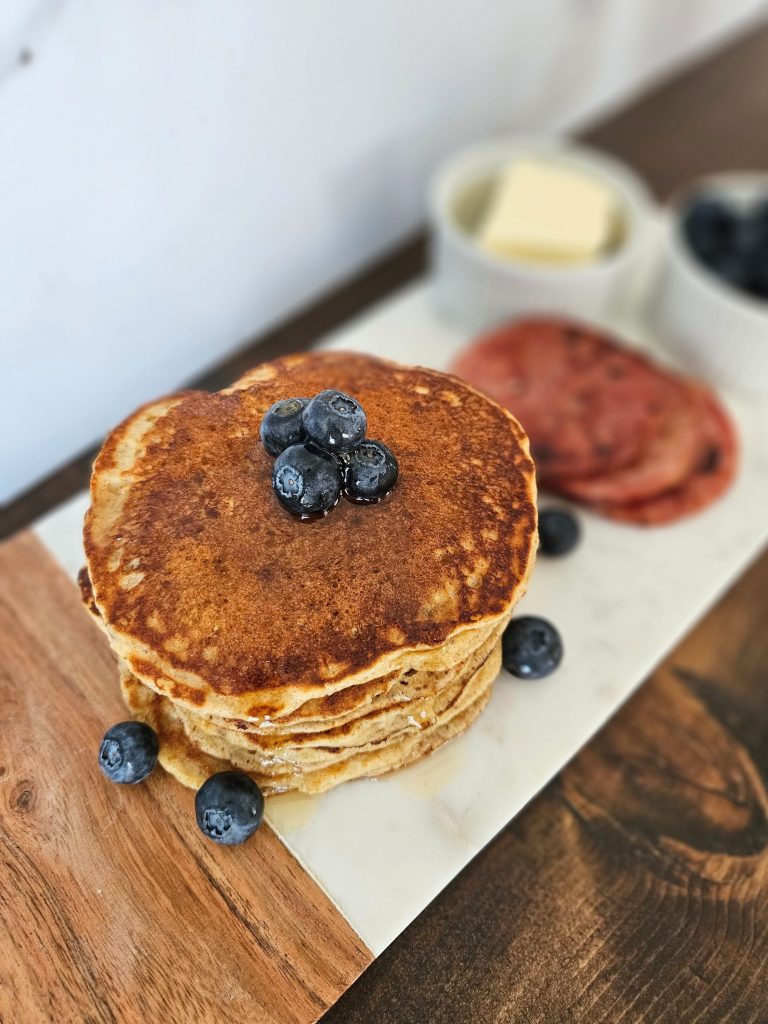 stack of einkorn pancakes with bacon and butter and blueberries on a white marble tray