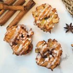 three sourdough discard apple fritters on a white counter top with cinnamon sticks