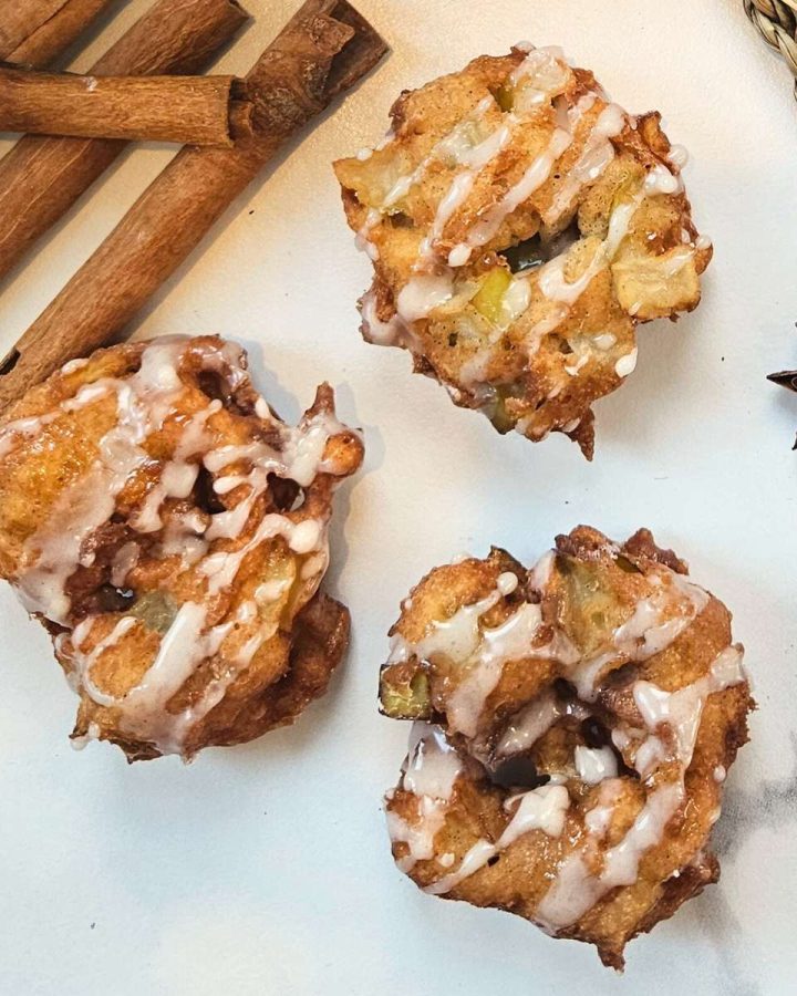three sourdough discard apple fritters on a white counter top with cinnamon sticks